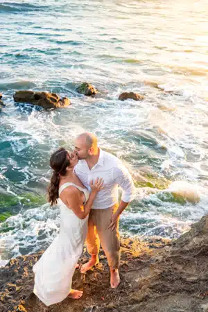 Sunset beach wedding photography: Couple kissing by ocean waves.