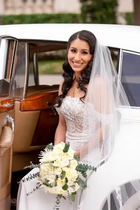 Bride smiling in a classic wedding car with bouquet