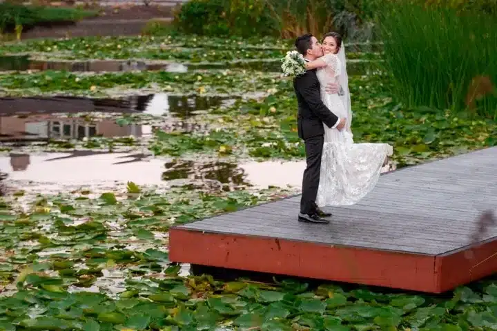 Bride and groom embracing on a dock by a lily pond.