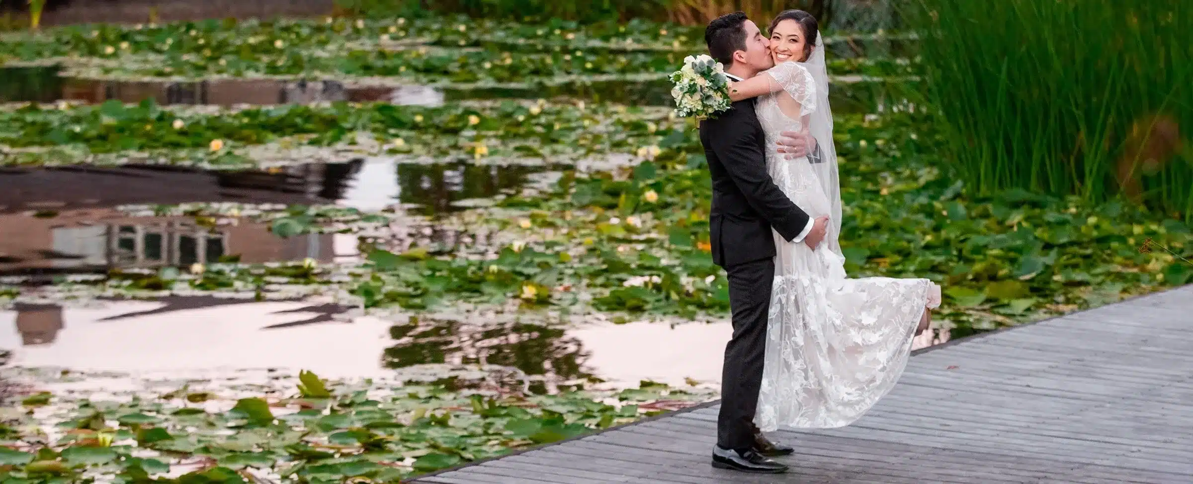Wedding photography: Groom lifting bride by a lily pad pond.